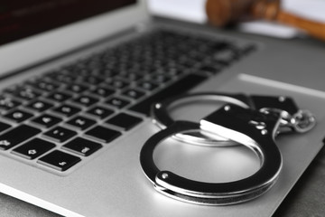 Laptop and handcuffs on table, closeup. Cyber crime