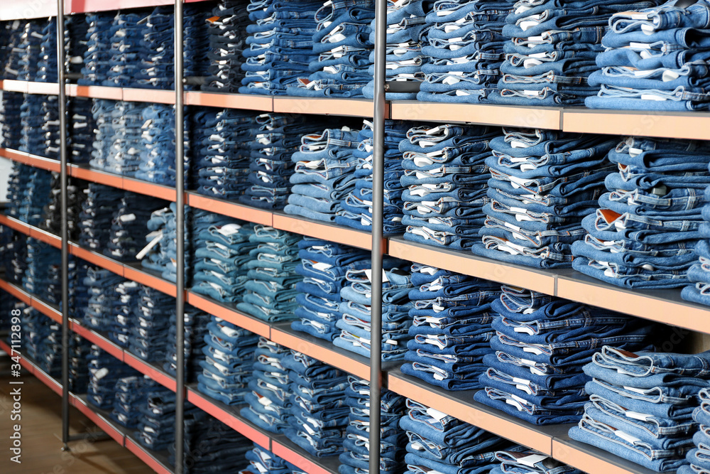 Wall mural Collection of stylish jeans on shelves in shop