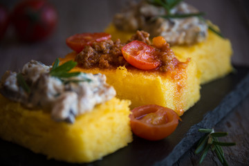 Slices of fried polenta with mushrooms and tomato sauce