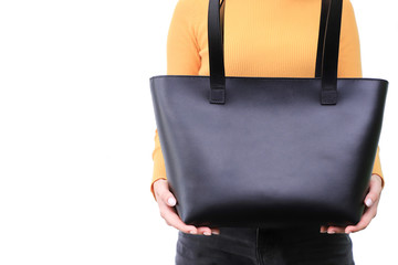 Handmade black bag is held by a girl with two hands in a yellow sweater and black jeans on a white background