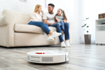 Family resting while robotic vacuum cleaner doing its work at home - obrazy, fototapety, plakaty