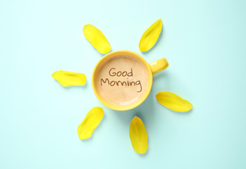 Cup of aromatic coffee and flower petals on light blue background, flat lay. Good morning