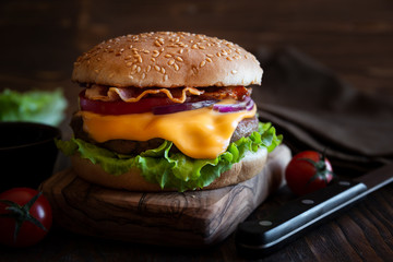Burger with cheese, bacon, tomato and lettuce on dark wooden background