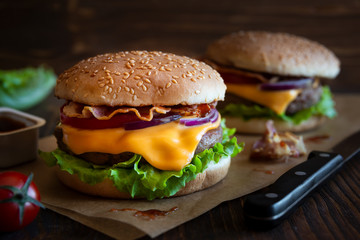 Burger with cheese, bacon, tomato and lettuce on dark wooden background