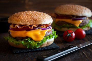 Burger with cheese, bacon, tomato and lettuce on dark wooden background