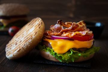 Burger with cheese, bacon, tomato and lettuce on dark wooden background