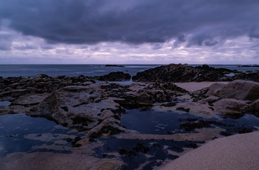 Rock pools on the beach at dusk. Long exposure. Dark moody sky.