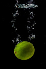 Fototapeta na wymiar whole and sliced green lime falling under water with a splash and bubbles on a white or black background