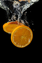 Obraz na płótnie Canvas whole and sliced orange falling under water with a splash and bubbles on a white or black background