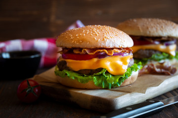 Burger with cheese, bacon, tomato and lettuce on dark wooden background