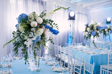 in the restaurant there are beautiful tables with tables, decor is made in blue, a wedding celebration, there are white chairs for guests, a huge vase with fresh flowers is on the table