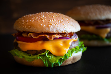 Burger with cheese, bacon, tomato and lettuce on dark wooden background