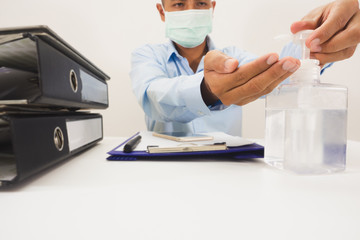 A white bottle of handwashing gel with the hands of a businessman sitting in a press to wash his hands before disinfecting work. On the desk, there were documents, phones, pens, taken from the front.
