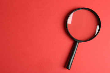 Top view of magnifying glass on red background, space for text. Search concept