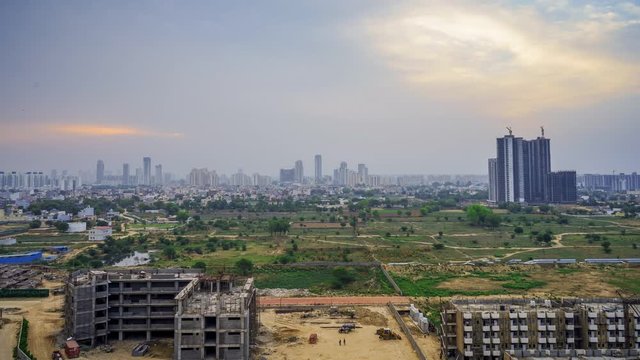 Aerial timelapse showing cityscape of gurgaon delhi india at sunrise with clouds, people moving on a construction site, showing empty feilds, slums, construction sites and sky scrapers in the distance