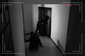 Dangerous criminals with gun and crow bar intruding into apartment, view through CCTV camera