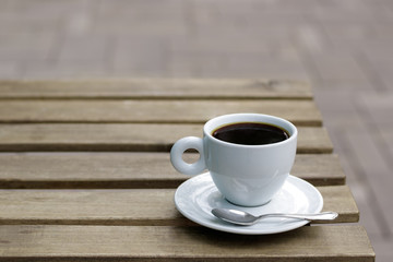 Coffee cup with tea spoon on wooden table on street