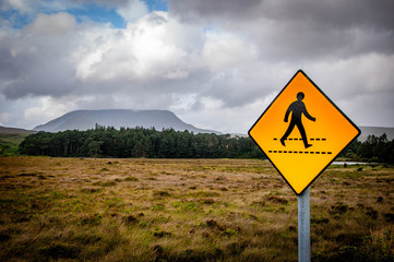 Irish pedestrian crossing roadsign in middle of wilderness next to flat topped Muckish Mountain in the Derryveagh range, County Donegal, Ireland