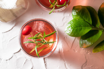 Glass of refreshing organic tea with cranberry and rosemary on white concrete background top view. 
