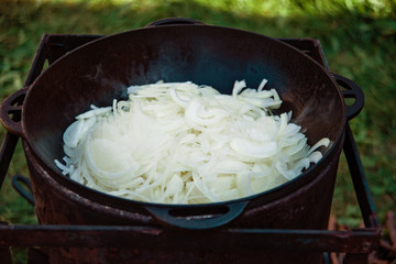Pilaf Cooking in cauldron on fire outdoors series. Pieces of onion on lamb meat are fried in...