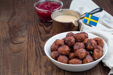 Meatballs in a white bowl, served with cream sauce and cranberry jam, swedish flag, horizontal, copy space