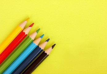 Colored pencils on yellow background. 6 colors Black, blue, blue, green, red, yellow. Pencils are well-honed. Flatlay. Isolated. Art. Art therapy. Leisure. Pencils placed in the lower left corner.