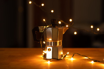 Pequeña maquina de café plateada puesta sobre la mesa decorada con luces amarillas