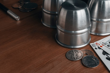 Set of professional tool to perform magic tricks on wooden table: three metal cups, some old coins, some playing cards and a magic wand