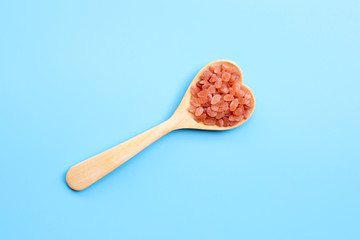 Pink himalayan salt in heart shape wooden spoon on blue background.