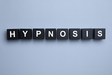 Black wooden blocks with word HYPNOSIS on light background, flat lay