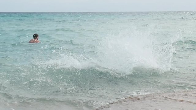 A man comes to the beach running and jumps into the water doing a dive. Then he goes out shaking his hair