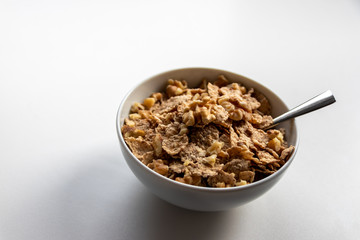 Porzellanschüssel mit gesundem Müsli, Cornflakes, Walnüssen und Löffel ist bereit fürs Frühstück mit Cerealien, Cornflakes und Müsli als gesunde Mahlzeit und Ernährung am Frühstückstisch