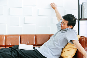An elderly Asian man is reading a book on the sofa in his house on a happy holiday..