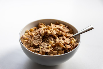 Porzellanschüssel mit gesundem Müsli, Cornflakes, Walnüssen und Löffel ist bereit fürs Frühstück mit Cerealien, Cornflakes und Müsli als gesunde Mahlzeit und Ernährung am Frühstückstisch