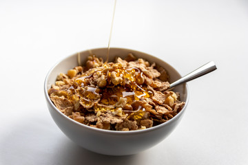 Schüssel mit gesundem Müsli, Cornflakes, Walnüssen, Honig und Löffel ist bereit fürs Frühstück mit Cerealien, Cornflakes und Müsli als gesunde Mahlzeit und Ernährung am Frühstückstisch