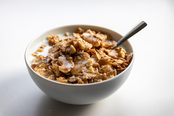 Schüssel mit gesundem Müsli, Cornflakes, Walnüssen, Honig, Milch und Löffel ist bereit fürs Frühstück mit Cerealien, Cornflakes und Müsli als gesunde Mahlzeit und Ernährung am Frühstückstisch