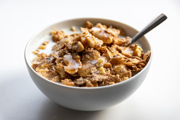 Schüssel mit gesundem Müsli, Cornflakes, Walnüssen, Honig, Milch und Löffel ist bereit fürs Frühstück mit Cerealien, Cornflakes und Müsli als gesunde Mahlzeit und Ernährung am Frühstückstisch