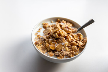 Schüssel mit gesundem Müsli, Cornflakes, Walnüssen, Honig, Milch und Löffel ist bereit fürs Frühstück mit Cerealien, Cornflakes und Müsli als gesunde Mahlzeit und Ernährung am Frühstückstisch