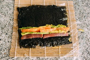 Making uramaki sushi with salmon, tuna, avocado rice and seaweed on a granite table.