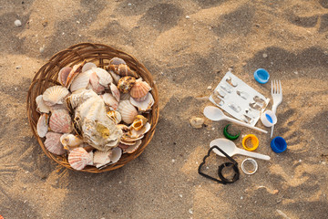 A lot of seashells in a basket on the sand, on the other sides , plastic garbage. The concept of choosing between beautiful nature and environmental pollution with plastic and garbage.