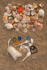 A lot of different plastic waste: disposable plastic cups,plastic bags, disposable spoons, forks, plastic lids, collected on the beach against the background of sand and beautiful shells. 