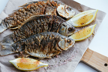National dish of river fish. Grilled carp, crucian carp with lemon slices and salt on a wooden board and craft paper on a black wood background