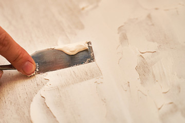 a small spatula applies putty to the wooden surface to create a structural background
