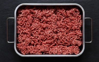 Photography of raw ground beef  in a metal bin on slate background for food illustration