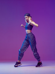 Cute teen girl dancing hip-hop in stylish clothes, a baseball cap, in a Studio with neon lighting....