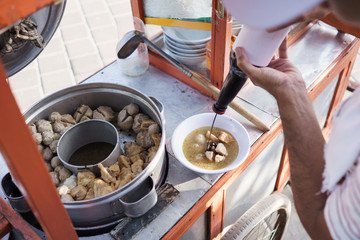 street food vendor of bakso or meatball. man pour some sweet soy sauce