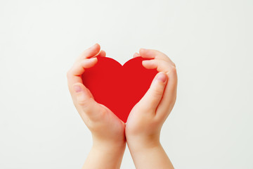 Fototapeta premium Paper red heart in hands of child on white background. Child love concept.