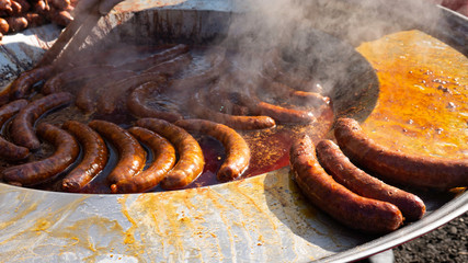 Tasty Sausages on Large Commercial Griddle Hotplate. Street Food Cooking on Big Frying Pan Outdoor. 