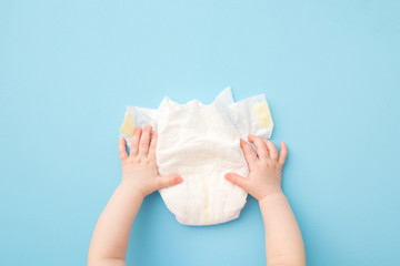 Baby hands touching white diaper on light blue table background. Pastel color. Closeup. Point of view shot. Top down view. - obrazy, fototapety, plakaty
