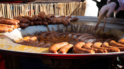 Festival of street food.  Sausages on Commercial Griddle Hotplate. Street Food Vendor Turning...